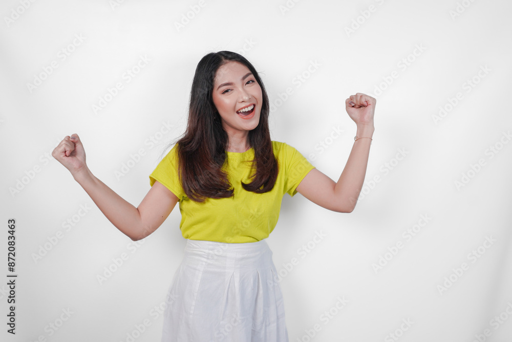 Φωτογραφία Cheerful Asian woman in a yellow shirt and white skirt is smiling and raising her arms in the air