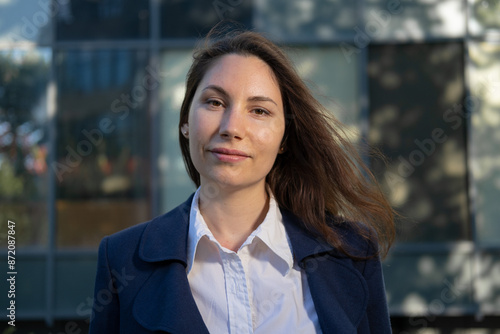 Portrait of an attractive strong confident independent woman in a blue suit standing against the background of a business building and looking at the camera