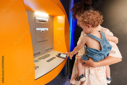 Hispanic Latin woman using ATM with her son in her arms during daytime photo