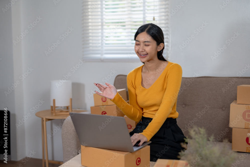 Woman working on laptop amid packages at home, representing e-commerce, online shopping, and home-based business operations. Woman working on laptop amid packages at home, representing e-commerce, online shopping, and home-based business operations.