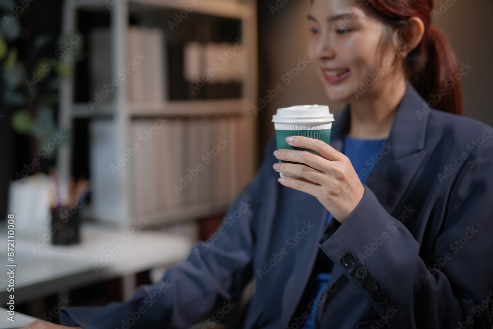 Businesswoman enjoying coffee while working on laptop in office. Focused and productive professional taking a break during busy workday. Businesswoman enjoying coffee while working on laptop in office. Focused and productive professional taking a break during busy workday.
