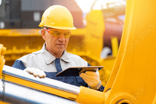 Machinery tractor mechanic with tablet computer checks hydraulic piston hose system equipment on excavator. Industrial service of mining truck