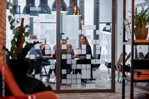 In a sleek glass office space, a team of business professionals engage in lively discussions and exchange strategic ideas, showcasing collaboration and innovation at the heart of modern corporate photo