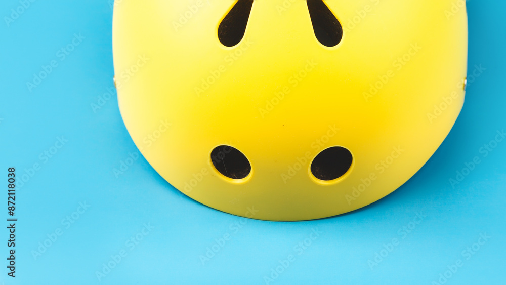 Fototapeta premium Yellow helmet on blue color background. Child's outdoors activity safety protection: rollers, bicycle, skateboard