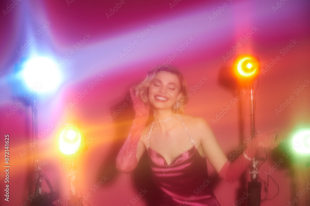 A woman in vibrant attire smiles brightly under the glow of colored spotlights. A woman in vibrant attire smiles brightly under the glow of colored spotlights.