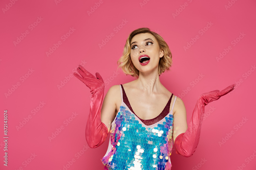 A woman in a sequined top and pink gloves poses against a pink background. A woman in a sequined top and pink gloves poses against a pink background.