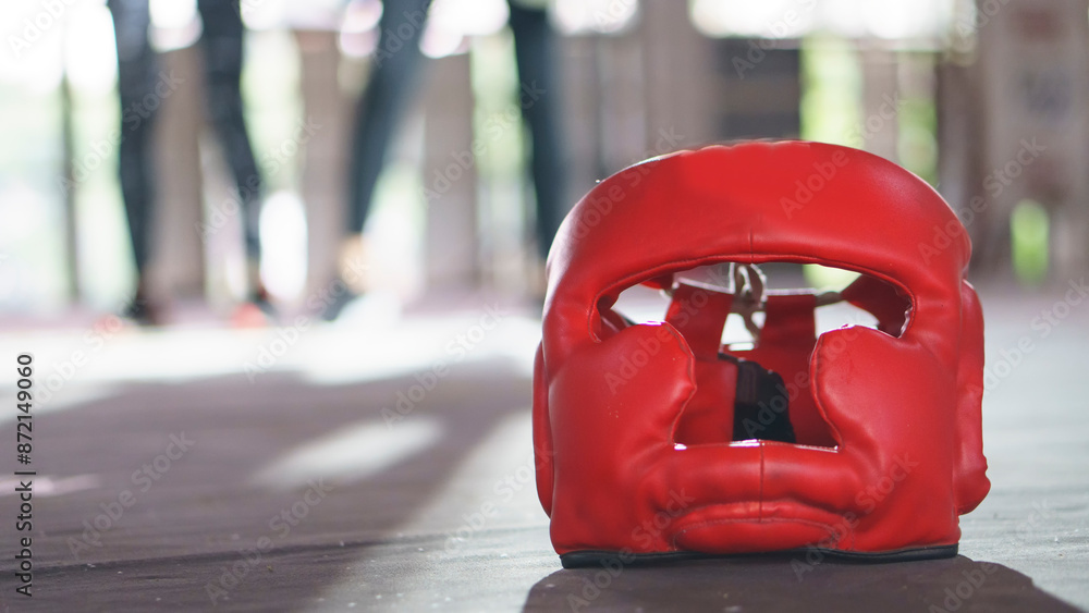 Obraz premium Boxing Headquard and leather mitt glove placed on canvas of ring in camp of training boxer. Equipments for protection during heavy sparring sessions, Used for Muay Thai, Kick Boxing and MMA Training