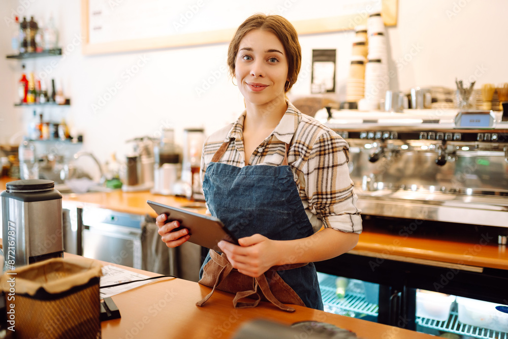 Young woman owner with tablet stands behind the counter of a coffee shop. Business concept. Takeaway food. Young woman owner with tablet stands behind the counter of a coffee shop. Business concept. Takeaway food.