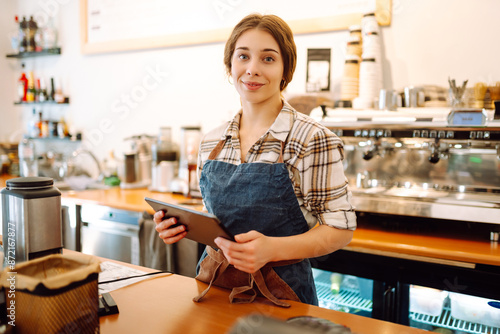 Young woman owner with tablet stands behind the counter of a coffee shop. Business concept. Takeaway food.