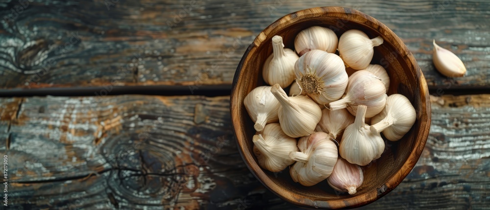 A wooden bowl overflowing with garlic sits on a weathered table, nearby are two garlic cloves A wooden bowl overflowing with garlic sits on a weathered table, nearby are two garlic cloves
