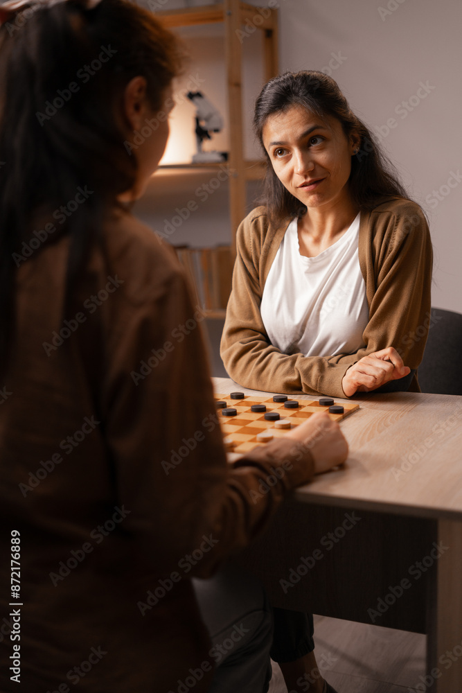 Two Women Engaged in Intense Checkers Game at Home, Board Game Leisure Activity Two Women Engaged in Intense Checkers Game at Home, Board Game Leisure Activity