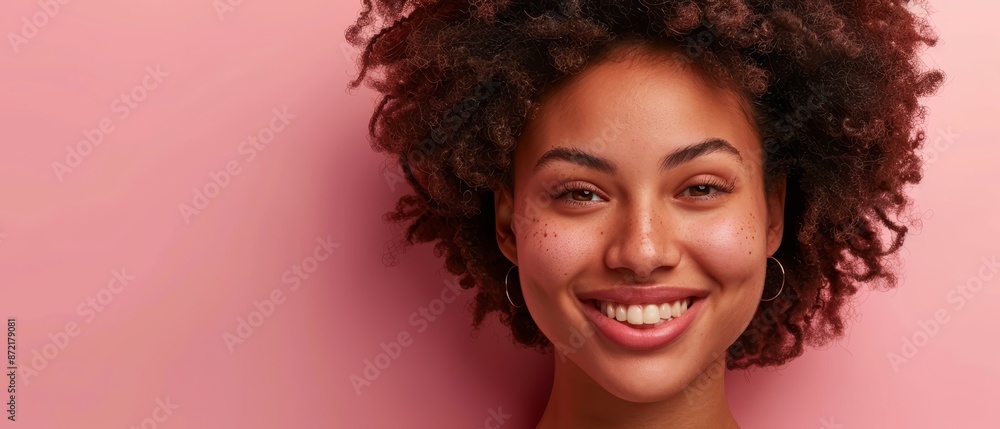 A close-up of a smiling woman with curly hair against a pink background A close-up of a smiling woman with curly hair against a pink background