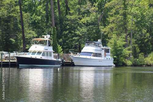 Two boats docked on a calm river with lush green trees in the background on a sunny day