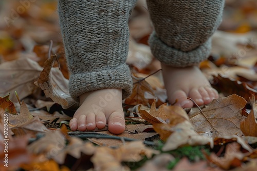 Close-up of a child's bare feet surrounded by orange autumn leaves in a forest park.