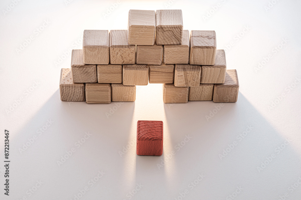 Obraz premium A single red wooden block stands out against a background of natural-colored wooden cubes arranged in an arch shape.