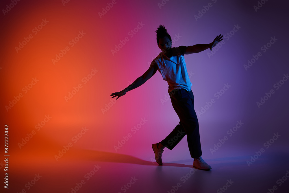 A young African American man dances with energy and grace against a vibrant gradient backdrop. A young African American man dances with energy and grace against a vibrant gradient backdrop.
