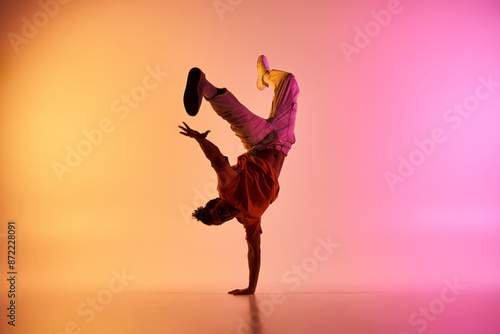 A Black man in a red shirt handstands with legs in the air against a colorful pink-orange backdrop.