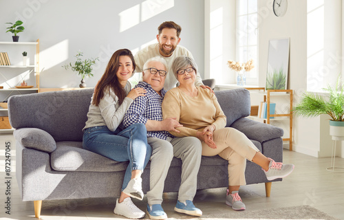 Family portrait capturing elderly parents and adult children embracing, sitting together on the sofa at home. This happy moment shows the love and bond between grandparents and family.