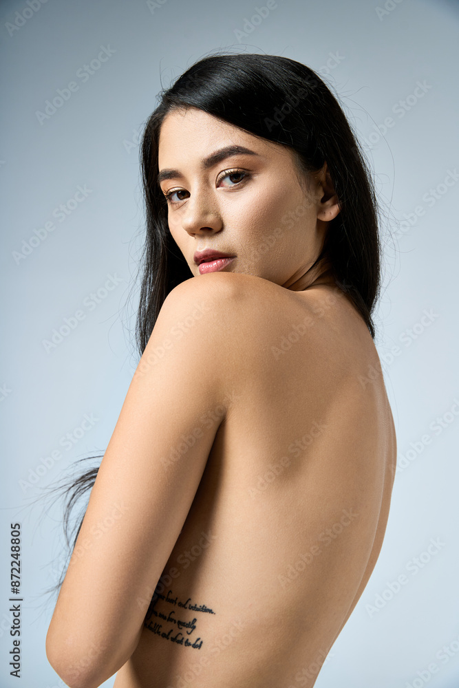 Young woman in studio with long black hair, back to camera, gazes over shoulder. Young woman in studio with long black hair, back to camera, gazes over shoulder.