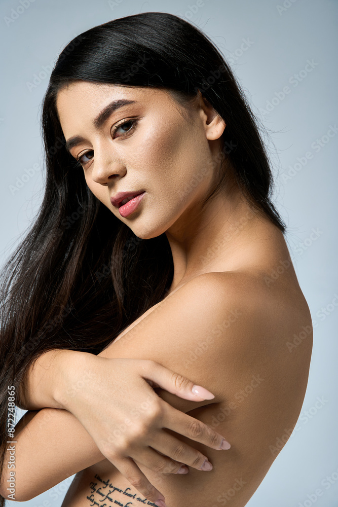 Naklejka premium A young woman with long dark hair poses with her arms crossed against a soft blue background.