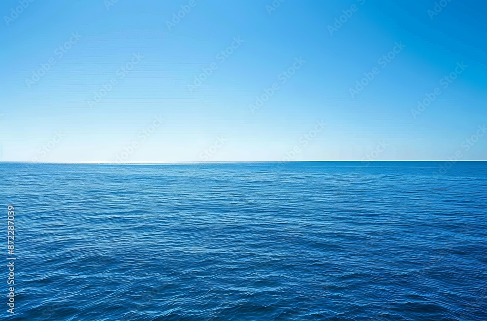 Fototapeta premium wide shot of the vast, calm sea under a clear blue sky. The water is a deep ocean color with gentle ripples and small waves in its distance