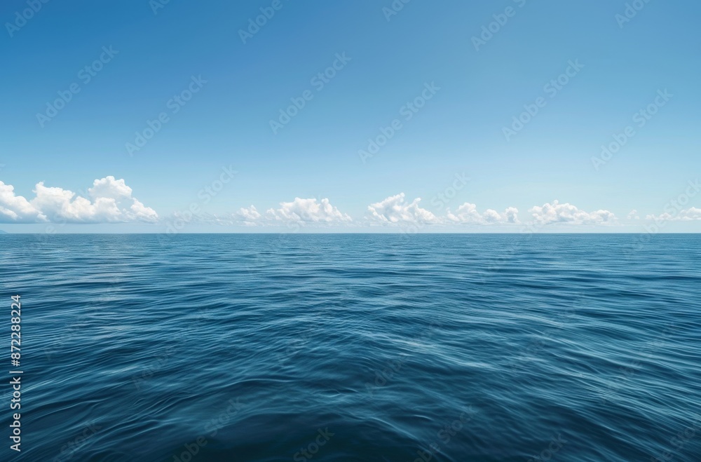 Fototapeta premium wide shot of the vast, calm sea under a clear blue sky. The water is a deep ocean color with gentle ripples and small waves in its distance