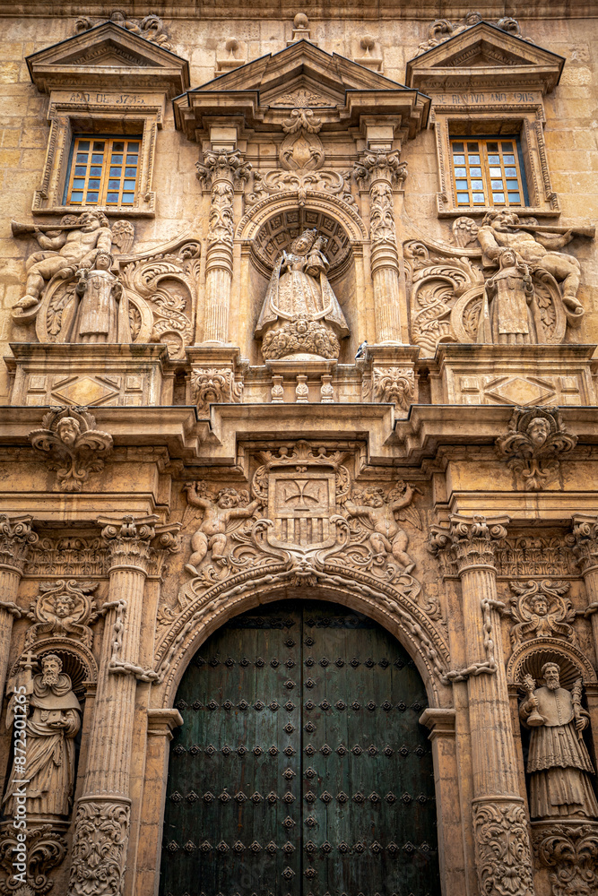 Vertical view of the baroque façade profusely decorated with columns and sculptures of saints of the church of La Merced, next to the university of Murcia, Spain