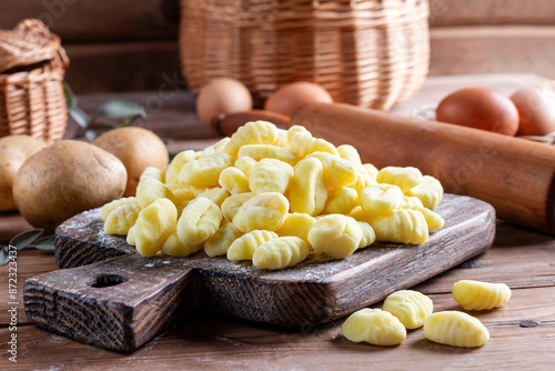 Uncooked homemade potato gnocchi on cutting board over wooden table with flour. See series.