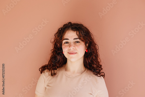 Potrait young woman with curly redhead and freckles looking at camera with natural expression. Orange pink background