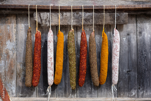 Variety of colorful cured sausages hanging against wooden backdrop