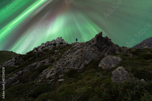 Lone anonymous traveler witnessing vibrant spring aurora over mountains