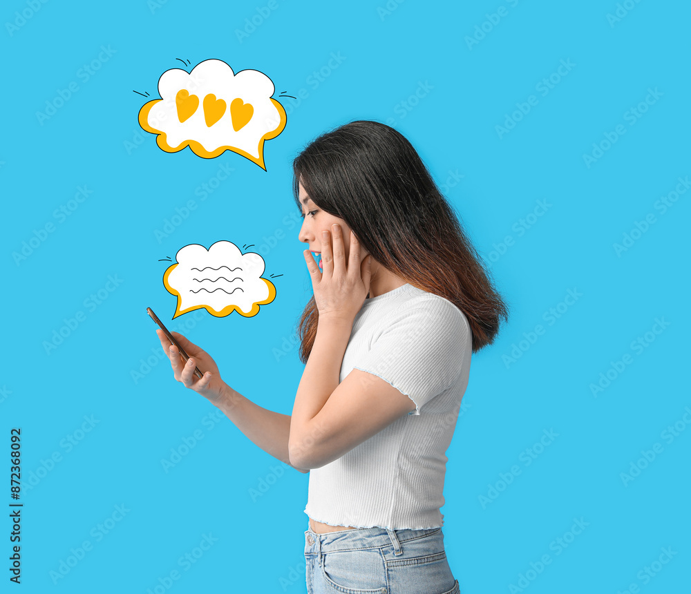 Surprised young Asian woman with mobile phone on blue background Surprised young Asian woman with mobile phone on blue background