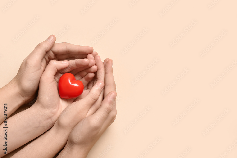 Hands of woman and child with red heart on beige background Hands of woman and child with red heart on beige background