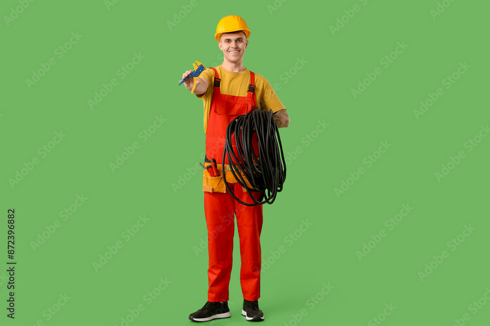 Young male electrician with wire stripper and flexible conduit tube on green background Young male electrician with wire stripper and flexible conduit tube on green background