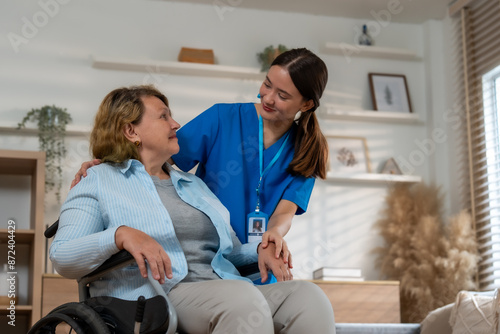 Caring Nurse Assisting Elderly Woman in Wheelchair at Home, Providing Compassionate Home Care in a Comfortable Living Room Setting photo