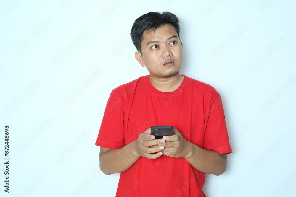 Young Asian man think something while typing on his mobile phone. Wearing red a shirt Young Asian man think something while typing on his mobile phone. Wearing red a shirt