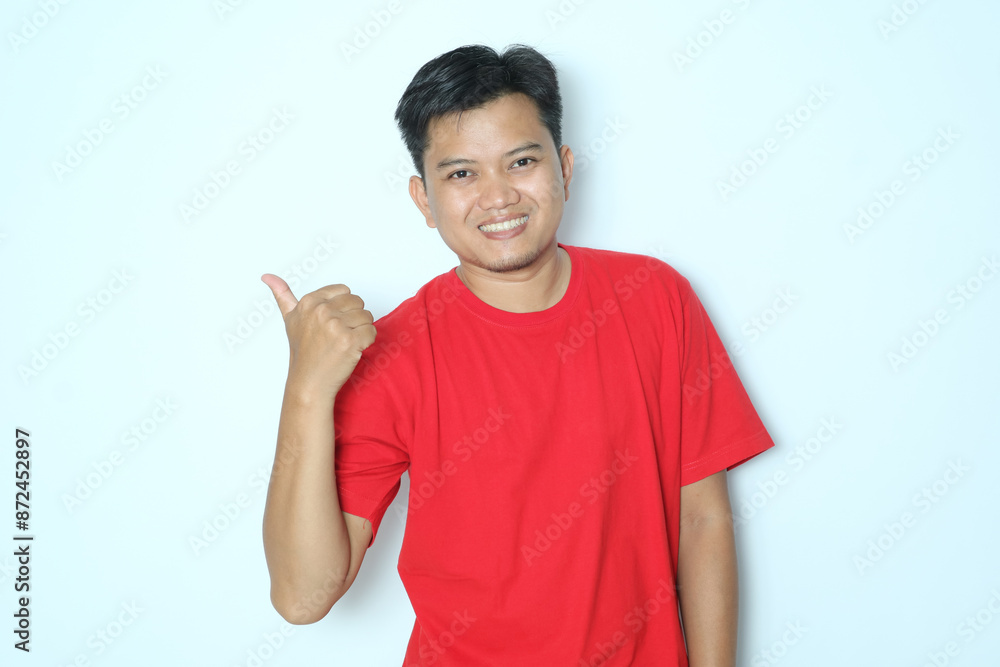 Young Asian man smiles and pointing to the right side with his thumb. Wearing red a shirt Young Asian man smiles and pointing to the right side with his thumb. Wearing red a shirt