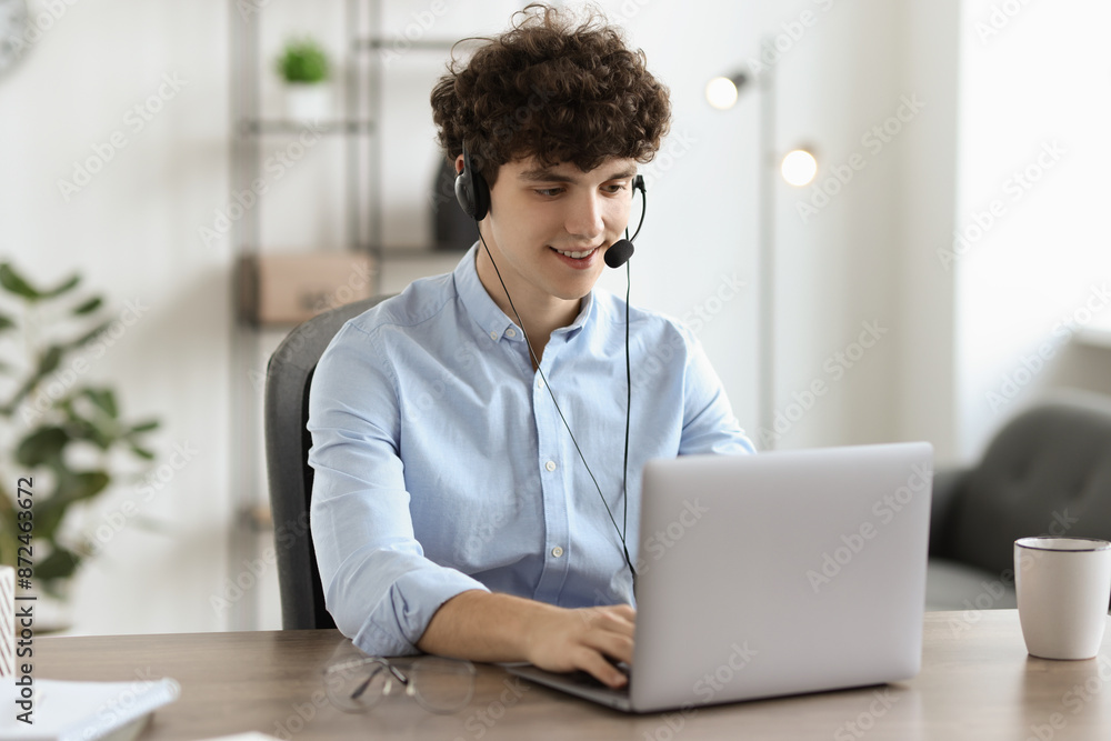 Teenager in headset working with laptop at table indoors. Remote job Teenager in headset working with laptop at table indoors. Remote job