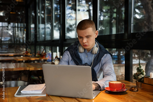 Young male student with laptop studying at table in cafe