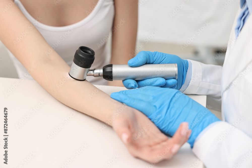 Dermatologist with dermatoscope examining patient at white table in clinic, closeup Dermatologist with dermatoscope examining patient at white table in clinic, closeup