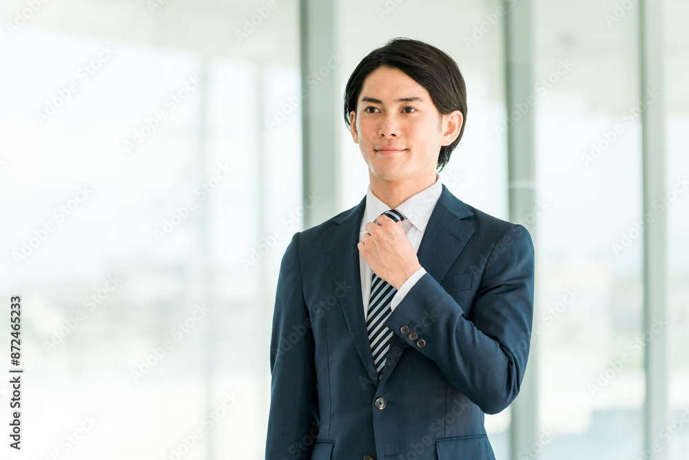 身だしなみ・ネクタイを整えるスーツ姿の若いアジア人ビジネスマン
