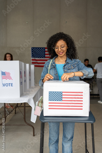 vertical portrait of a young african american woman voting in the us election, placing vote ballot in the polling box, vote in America. Concept of usa choice, democracy and freedom