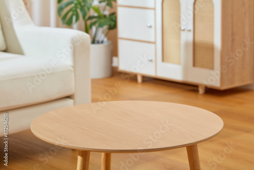 The wooden table in the living room with modern style, which placed on the wooden parquet, in the back is a white sofa and white cabinet. Empty space for product showing and adding elements of design