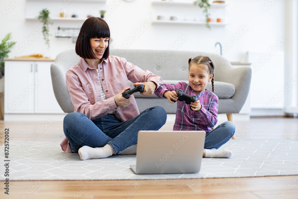 Mother and daughter sitting on floor playing video games using game controllers. Both smiling and engaging in fun activity together in cozy living room setting. Mother and daughter sitting on floor playing video games using game controllers. Both smiling and engaging in fun activity together in cozy living room setting.