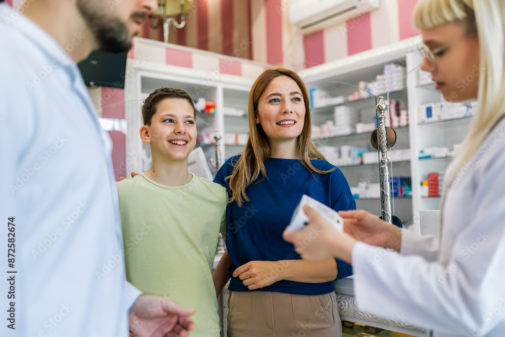 Cheerful pharmacist chemist man and woman giving vitamins to young mom and her son. Cheerful pharmacist chemist man and woman giving vitamins to young mom and her son.