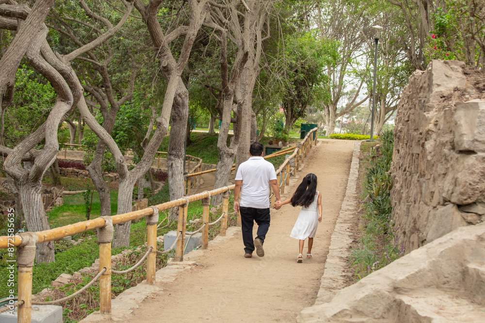 Fototapeta premium Family members holding hands while walking in a park during a sunny day in Lima Peru