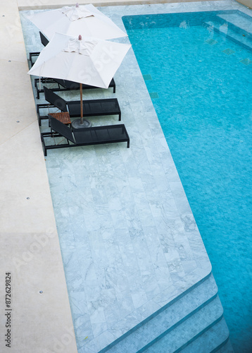 Top view of luxury swimming pool with lounge chairs and white umbrella at a modern resort. High angle view of a turquoise swimming pool and black sun loungers at a luxury hotel.