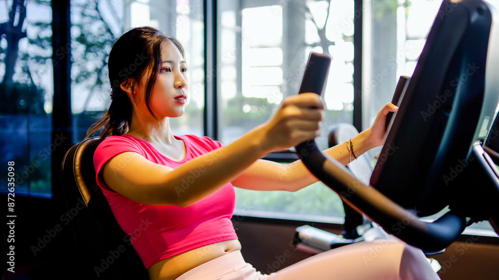 Young Asian woman to step on flywheel training helping leg muscle strength, Healthy girl training or a quick warm up in the fitness room. lifestyle or health of female Young Asian woman to step on flywheel training helping leg muscle strength, Healthy girl training or a quick warm up in the fitness room. lifestyle or health of female