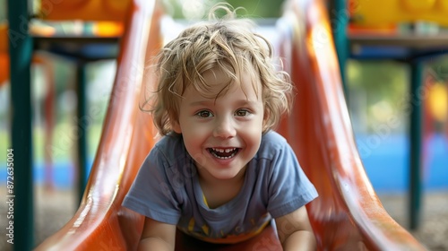 Happy preschooler boy playing on a slide on the playground in summer. copy space for text. © Naknakhone