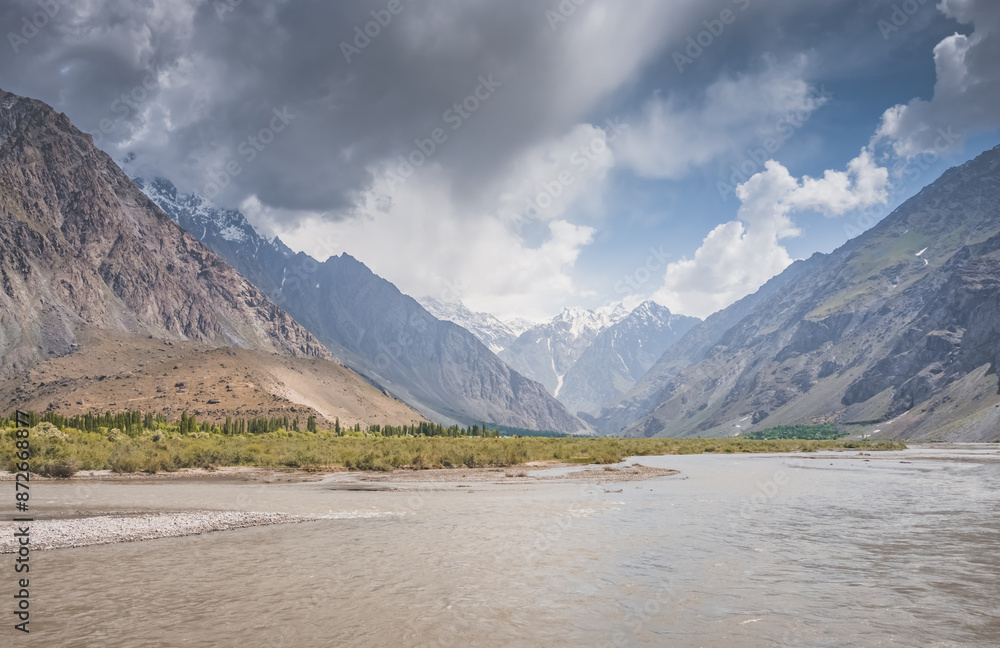 Mountain wide and noisy Panj river flows in Wakhan valley corridor between peaks and mountains against rocky Tien Shan range in Pamir in Tajikistan Mountain wide and noisy Panj river flows in Wakhan valley corridor between peaks and mountains against rocky Tien Shan range in Pamir in Tajikistan